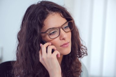Esmer kıvırcık saçlı Genç iş kadını bir telefon görüşmesi geçiriyor.