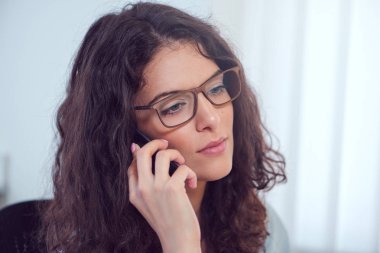 Esmer kıvırcık saçlı Genç iş kadını bir telefon görüşmesi geçiriyor.