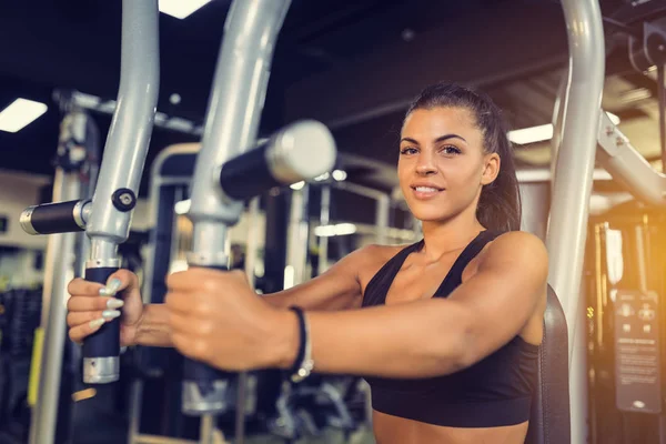 Young woman training upper body using fly machine