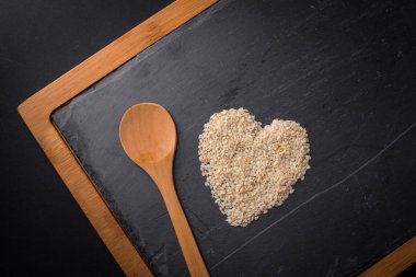 Uzun saplı bir tahta kaşık susam ile doldurulur. Kalp. -Yemek, vejetaryenlik, sağlıklı yemek mutfak konsepti,.