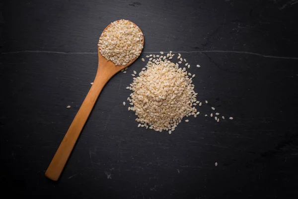 Stock image White sesame seeds in spoon on black granite backgroud