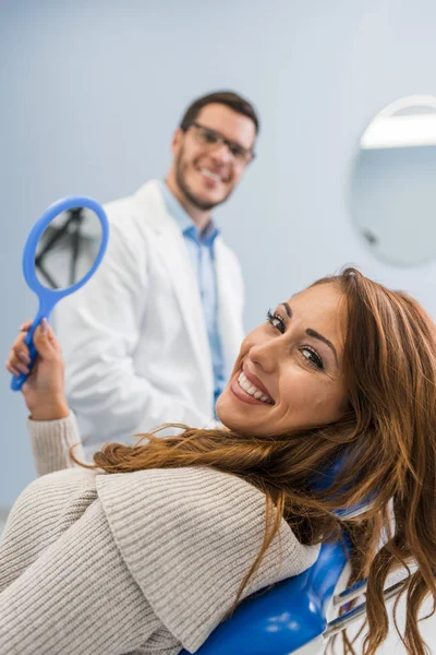 歯科用の椅子に座って 歯を鏡で見ている幸せな女患者 — ストック写真