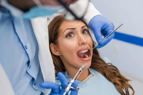 Woman looking scared as dentist puts syringe in his mouth