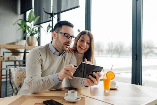 Beautiful couple having coffee on a date, using digital tablet and credit card for online shopping