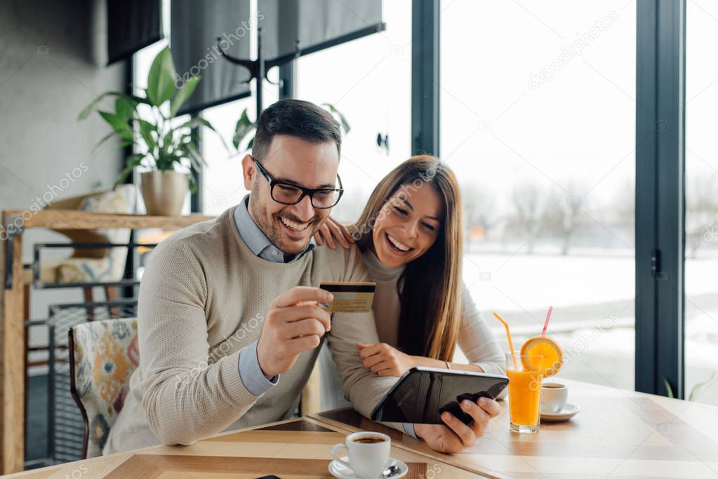 Young couple buying online with credit card and tablet in a coffee shop.