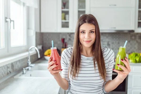 Young woman holding two smoothie bottles. Red and Green.