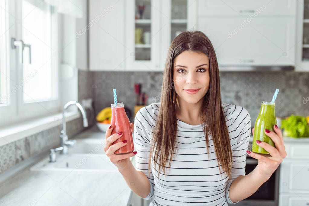 Young woman holding two smoothie bottles. Red and Green.