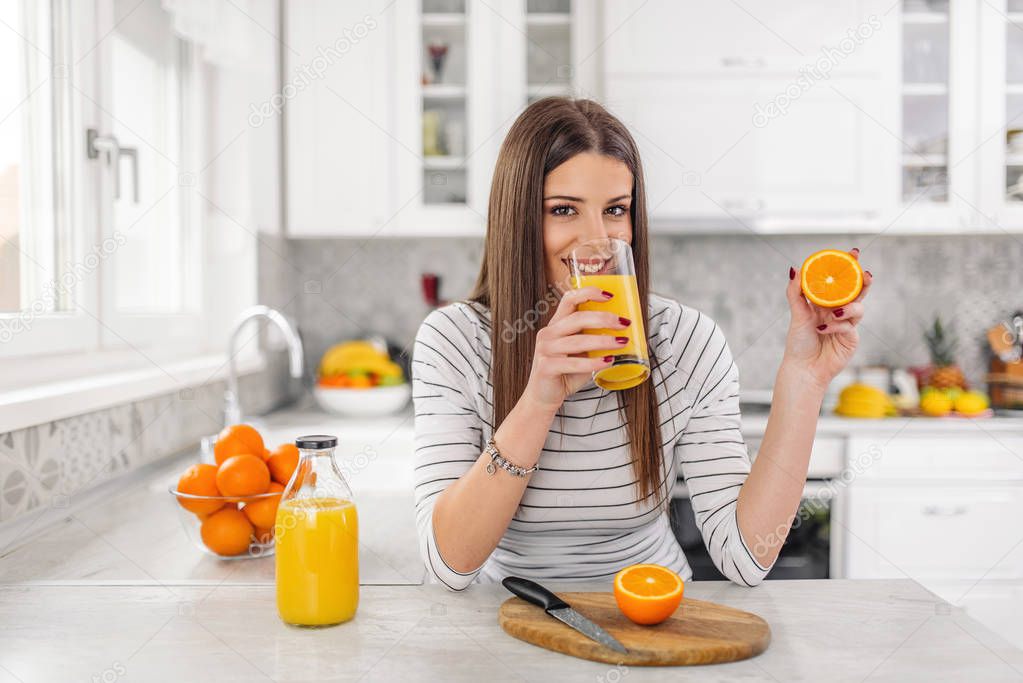 Close up Attractive young Woman drinking juice while Holding Sliced Orange Fruit.