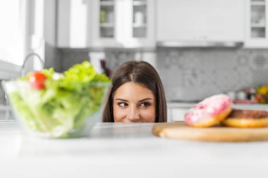 Diet. Dieting concept. Healthy Food. Beautiful Young Woman choosing between Salad and Sweets clipart