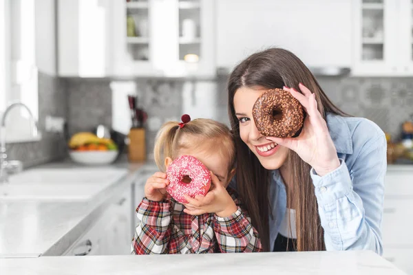 Madre y su hija se están divirtiendo con rosquillas de colores. Concepto de dieta y comida chatarra . — Foto de Stock