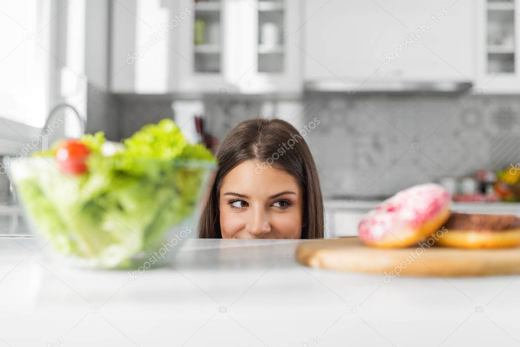 Diet. Dieting concept. Healthy Food. Beautiful Young Woman choosing between Salad and Sweets