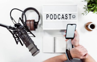 Müzik stüdyosunda cep telefonu tutan ellerin üst görünümü. Podcast kavramı.