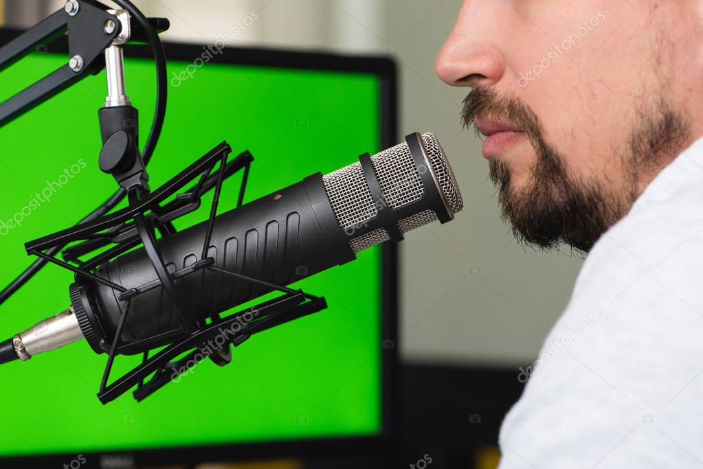 Man talking into a microphone during a podcast recording. Green screen