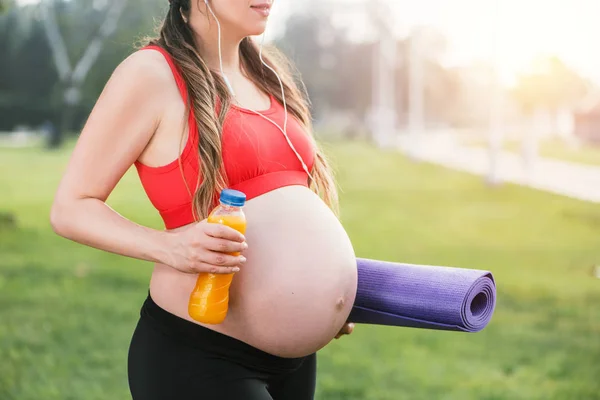 Eine Frau im roten T-Shirt geht mit Sportflasche und Yogamatte in der Hand durch den Park — Stockfoto