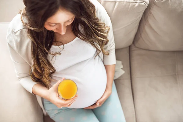 Vue du dessus de la femme enceinte heureuse buvant ou tenant du jus d'orange à la maison Images De Stock Libres De Droits