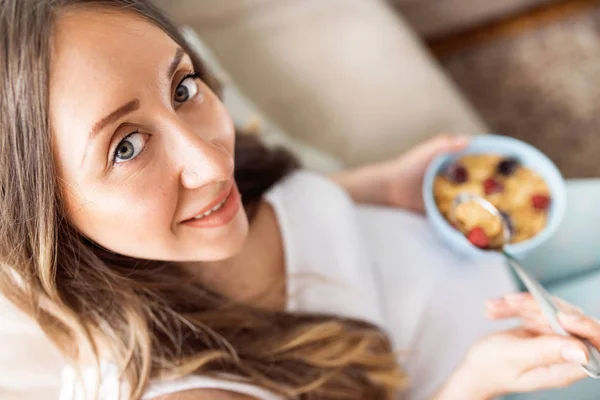 Gros plan de la femme enceinte heureuse mangeant des céréales avec des fruits pour le petit déjeuner au lit à la maison. Regardant la caméra Images De Stock Libres De Droits