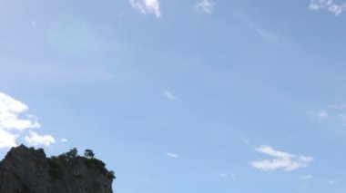 Bulanık zaman kayalıkları gündüz vakti kayalık kayalıklara çarpıyor. Arka planda mavi gökyüzü ve bulutlarla.