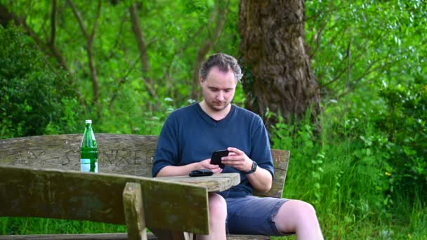 Egy Férfi Egy Padon Természetben Élvezi Nyári Napot Használja Mobilját — Stock videók