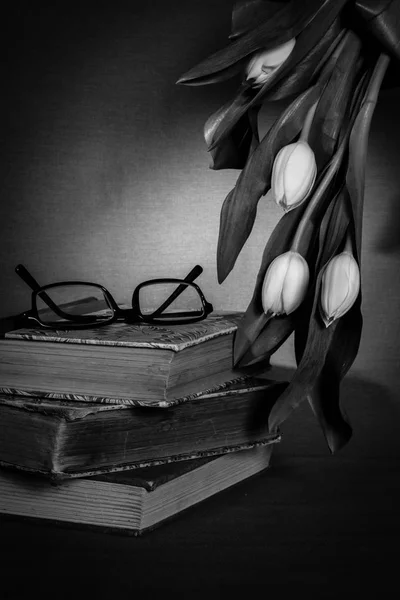 Pile of old books with pair of glasses and white tulips — Stock Photo, Image