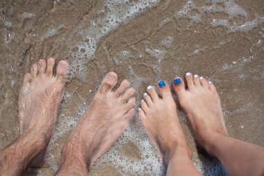 Kumlu bir sahilde erkek ve kadın ayakları. Tatil konsepti.