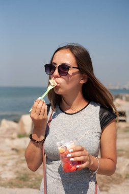 Deniz kıyısındaki kız bardakta meyve tatlısı yiyor..