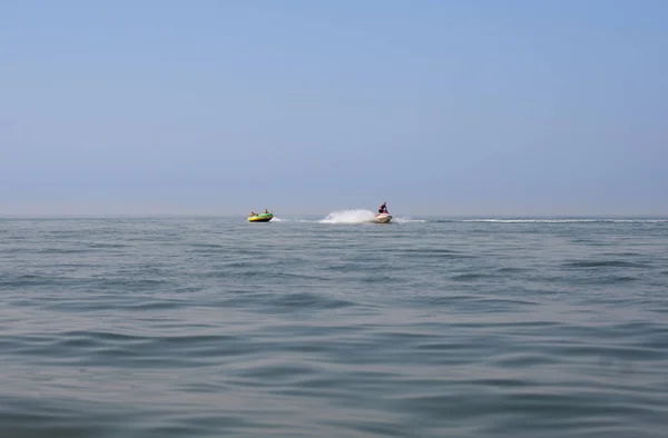 Two mans on bouncing tube having  being towed by a speeding boat.