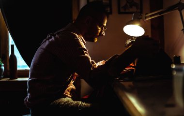 Avrupalı adam evde ki dikiş atölyesinde elbise dikiyor.