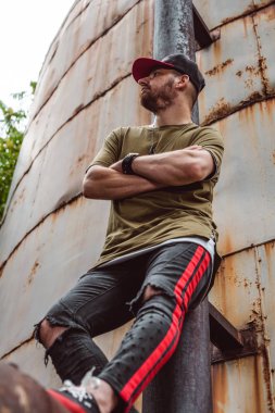 Şık giyimli adam, terk edilmiş bir yerde paslı bir arka plan üzerinde.