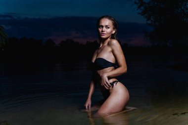 Suda güzel bir model. Gece için siyah bikini mayo, yüzme ve poz.