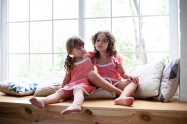 Evde küçük kızlar pencerenin yanında gecelik le. Yastıklarla rahatça oturun.