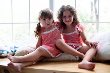 Evde küçük kızlar pencerenin yanında gecelik le. Yastıklarla rahatça oturun.