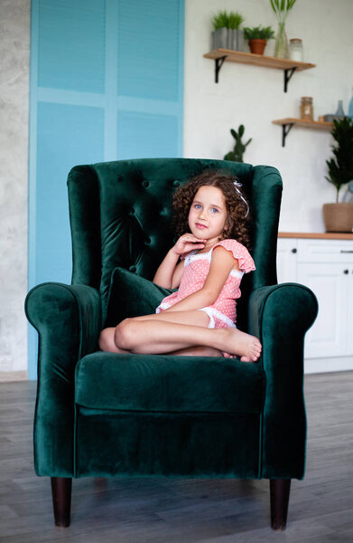 A little girl sits in a large armchair for adults. Velor, green, chic armchair.