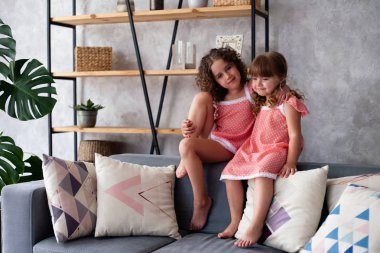 Küçük kızlar bir sürü yastıkla kanepede oturuyorlar. Gecelikle.