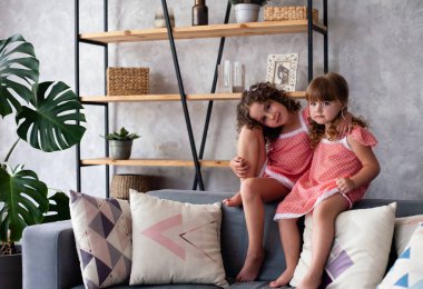 Küçük kızlar bir sürü yastıkla kanepede oturuyorlar. Gecelikle.