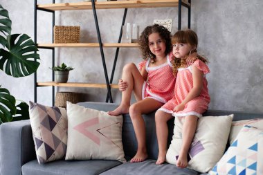 Küçük kızlar bir sürü yastıkla kanepede oturuyorlar. Gecelikle.