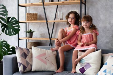 Küçük kızlar bir sürü yastıkla kanepede oturuyorlar. Gecelikle.