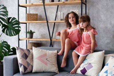 Küçük kızlar bir sürü yastıkla kanepede oturuyorlar. Gecelikle.