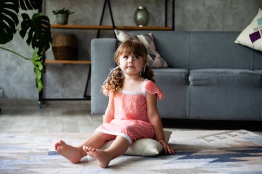 Küçük kız yerde yastık oturuyor. Gecelikle.