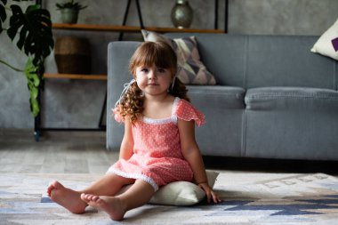 Küçük kız yerde yastık oturuyor. Gecelikle.