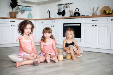 Küçük kızlar yerde otururken mutfakta oynanır.
