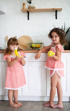Mutfakta meyveli iki küçük kız. Sağlıklı gıda ile buzdolabı yakınında Çocuklar.