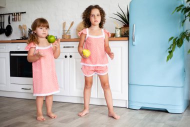 Mutfakta meyveli iki küçük kız. Sağlıklı gıda ile buzdolabı yakınında Çocuklar.