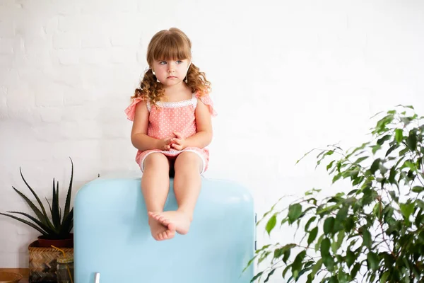 小さな女の子が冷蔵庫に座っている 青い色の美しいレトロな冷蔵庫に座って スタイリッシュなインテリア — ストック写真