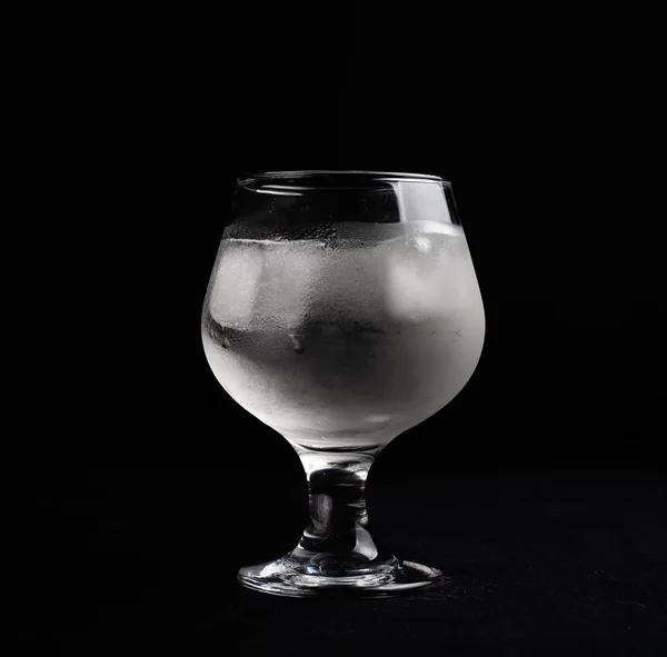 A misted glass with ice on a dark background.