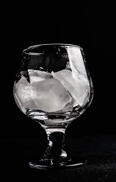 A misted glass with ice on a dark background.