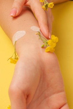 El sanatları, doğal kozmetik kadınları, sarı güzel kadınlar, bahar çiçekleri, parlak kontrast makyajlı eller, el bakımı. Moda, yaratıcı fotoğrafçı kız masada oturuyor, sarı zıt arkaplan. Yukarıdan bak, yakın plan..