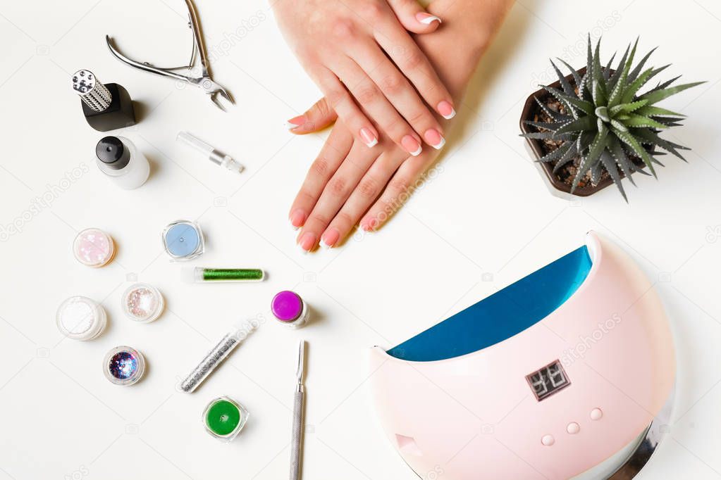 Composition for nail care, female young hands, French manicure, gel polish, lamp for nails and equipment for nail care. Flat lay photo.