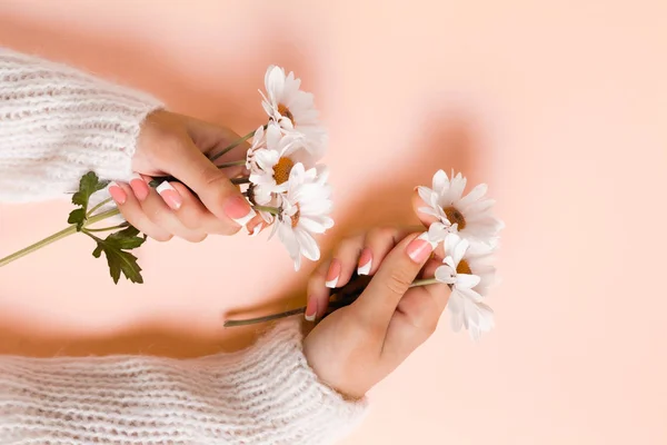 Slender young hands hold flowers, with a thin wrist, clean skin and French manicure. Flat lay photo, with place for text.