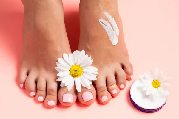 Woman\'s perfect, groomed feet with of natural herbal cream. Love a feet. Beautiful flowers on pink background. Care about clean, soft and smooth skin on foot. Fresh flowers.