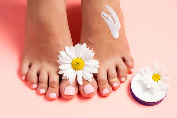 Woman\'s perfect, groomed feet with of natural herbal cream. Love a feet. Beautiful flowers on pink background. Care about clean, soft and smooth skin on foot. Fresh flowers.